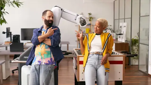Dois associados em frente a uma mesa de matraquilhos com um robô de assistência Bosch Rexroth APAS.
